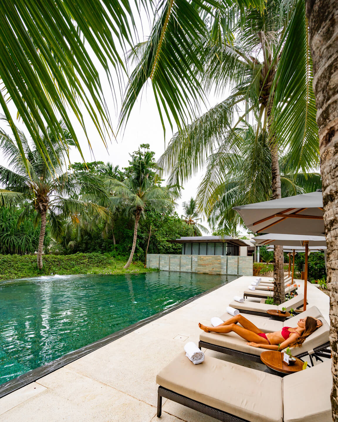 girl relaxing at a pool in The Maldives surrounded by palm trees