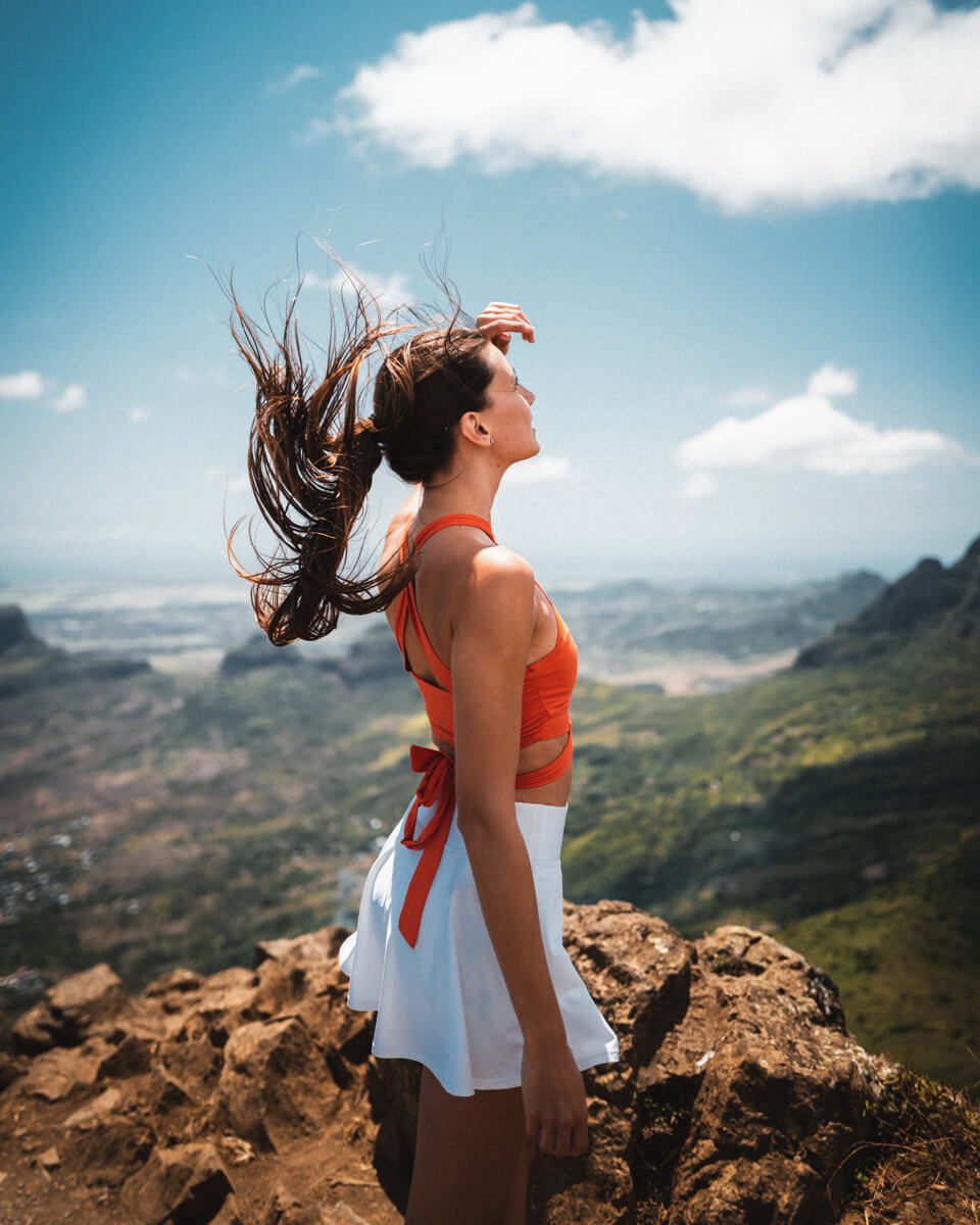 a Girl Standing on the top go the le pouce mountain in Mauritius , enjoying the view after the hike, while the wind blows through the hair