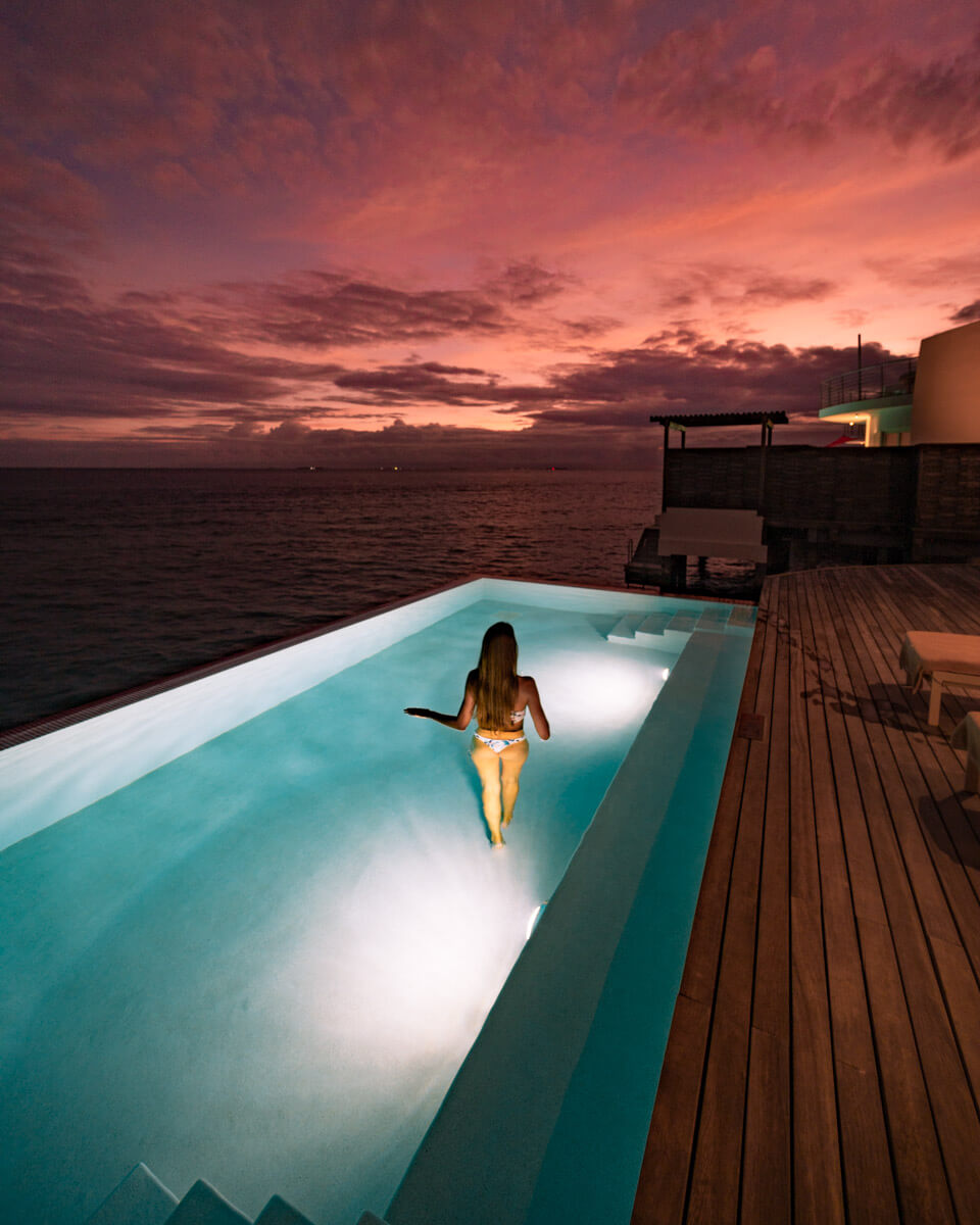 girl standing in a pool at night, watching the sunset at the water villa of the Jumeirah Maldives Olhahali Island