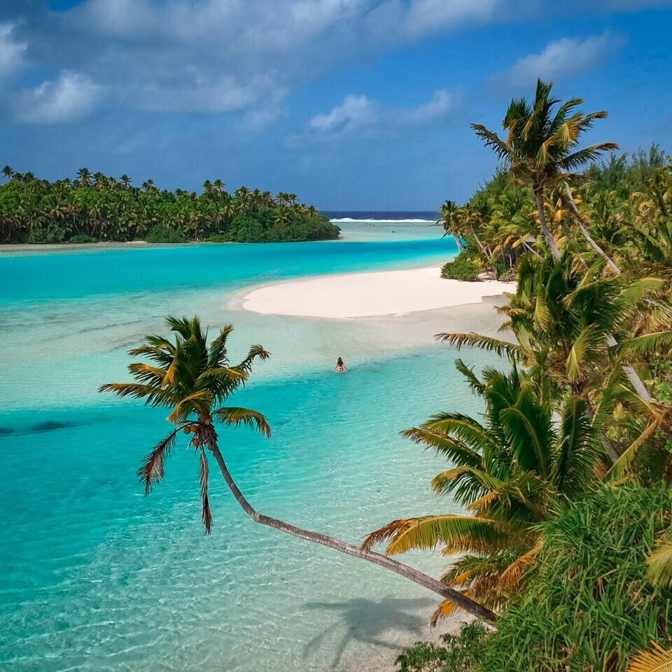 walking in the blue lagoon toward a beach between to islands, one foot island, Aitutaki