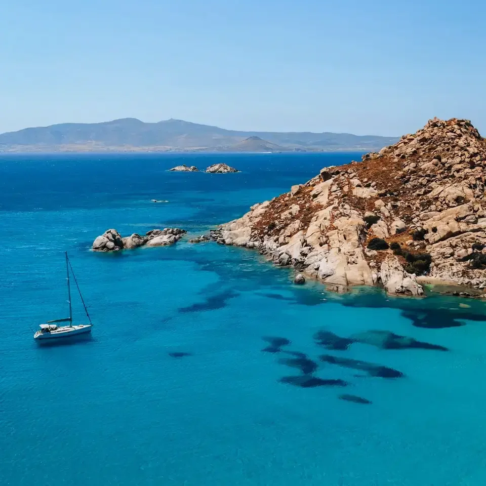 naxos-greece-island-hidden-gem aerial view over Naxos island in Greece, with blue water and a sailing boat in the sea