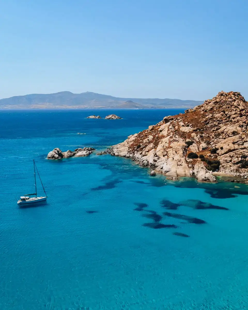 aerial view over Naxos island in Greece, with blue water and a sailing boat in the sea